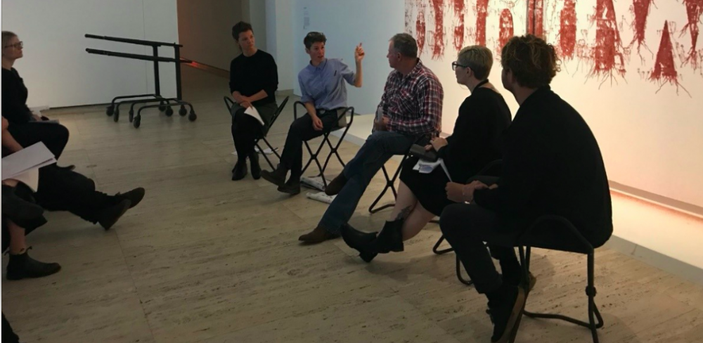Panel discussion with five people seated in a row looking at a speaker