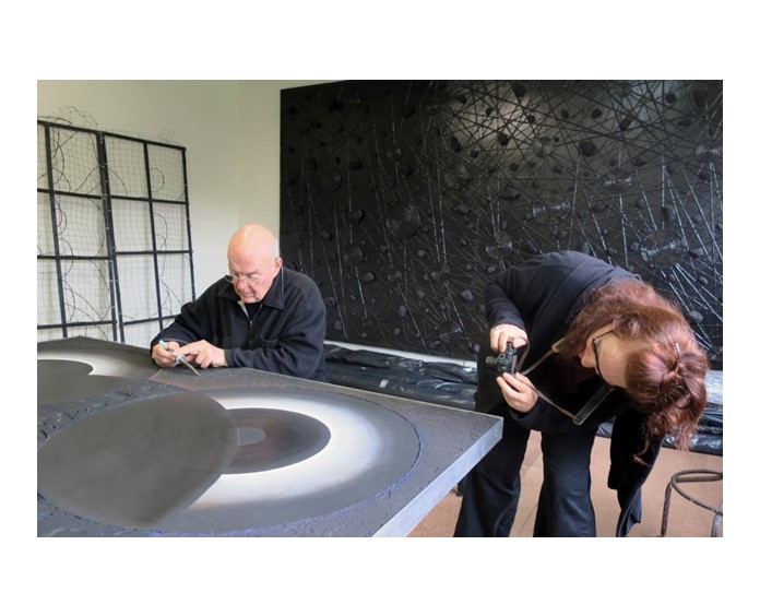 Asher Bilu working on ‘Graphite Light’ c.1970 in his Brighton studio as paintings conservator Lisa Nolan documents the repaired changes. Photo: MAGNT