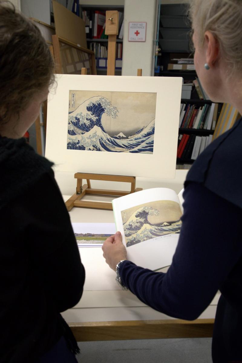 Ruth Shervington and Bonnie Hearn comparing the NGVs The great wave of Kanagawa, c. 1830,and an image of JUMs impression in the Paper and Photographs Conservation studio.