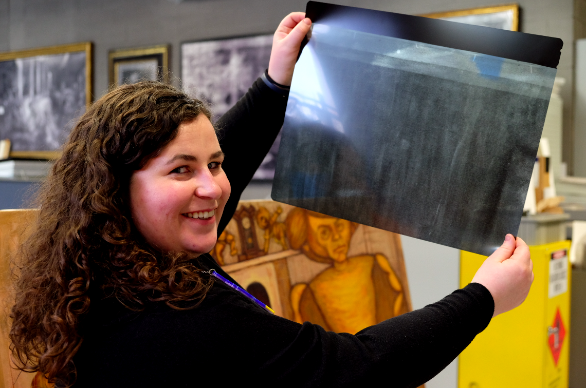 Murphy Bouma, Paintings intern, with one of the X-rays she produced from NGV Collection artwork John Perceval and his angels (1962) by John Brack.