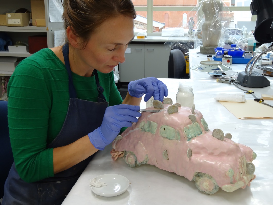 Megan Sypek treating a previously repaired ceramic car made by artist Margaret Dodd