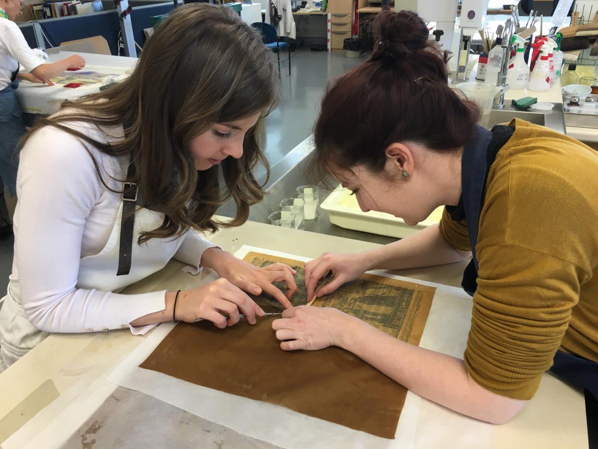 Freya Merrell and Sally Kilby painstakingly removing an acidic backing from a delicate newspaper item. Image: Rachel Sawicki