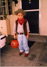 young boy wearing cowboy outfit holding artificial pumpkin