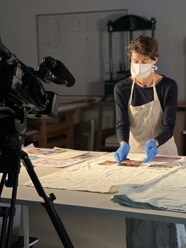 Conservator working on paper object wearing gloves and mask being filmed