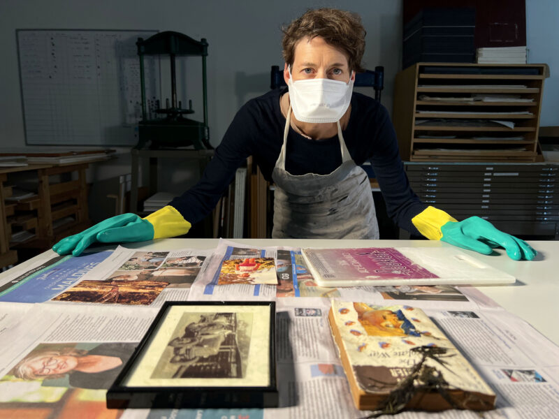 Conservator wearing mask and gloves leaning over table with works placed on drying paper